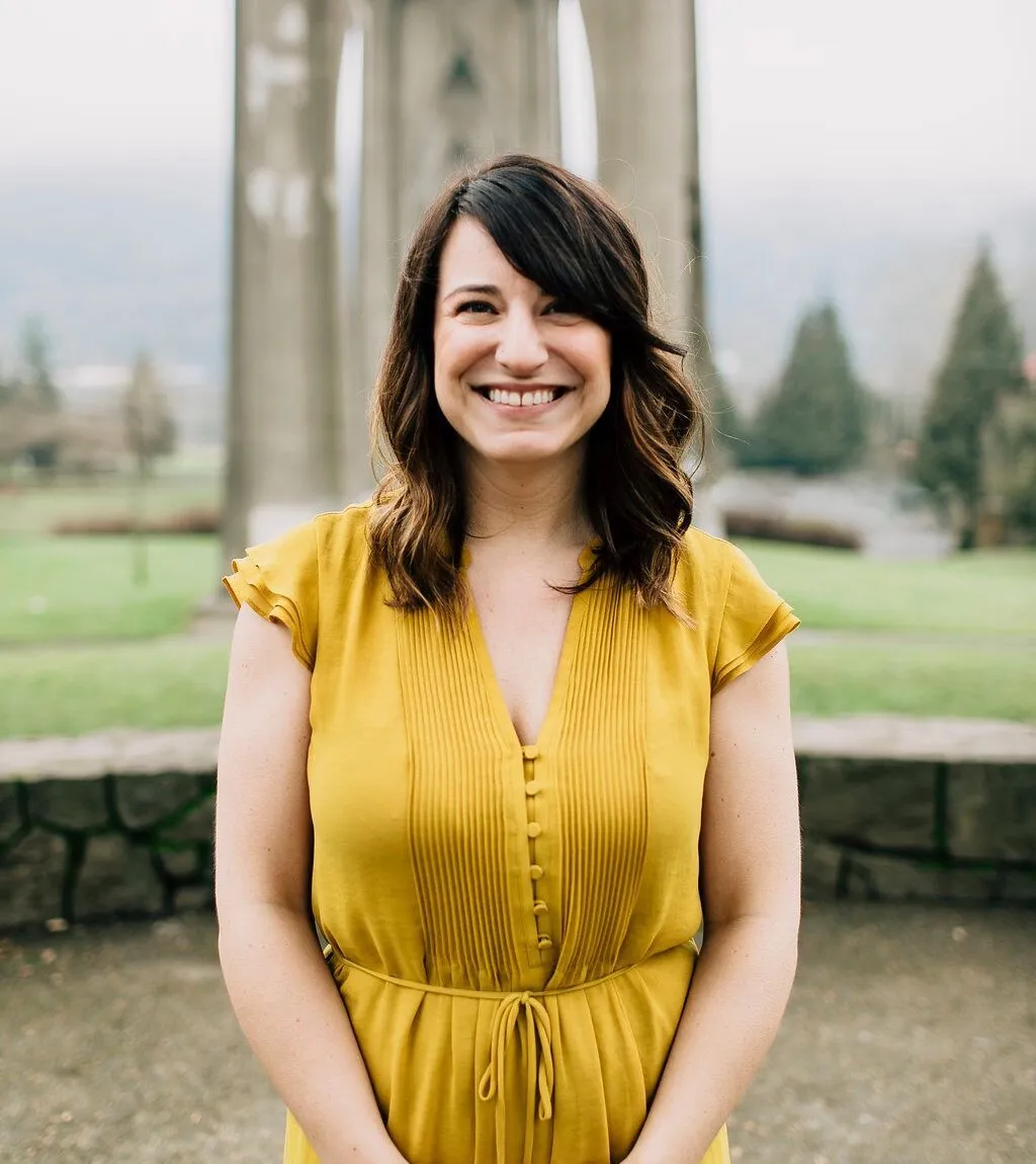 Kate Wille smiling in a yellow dress beneath the St. Johns Bridge